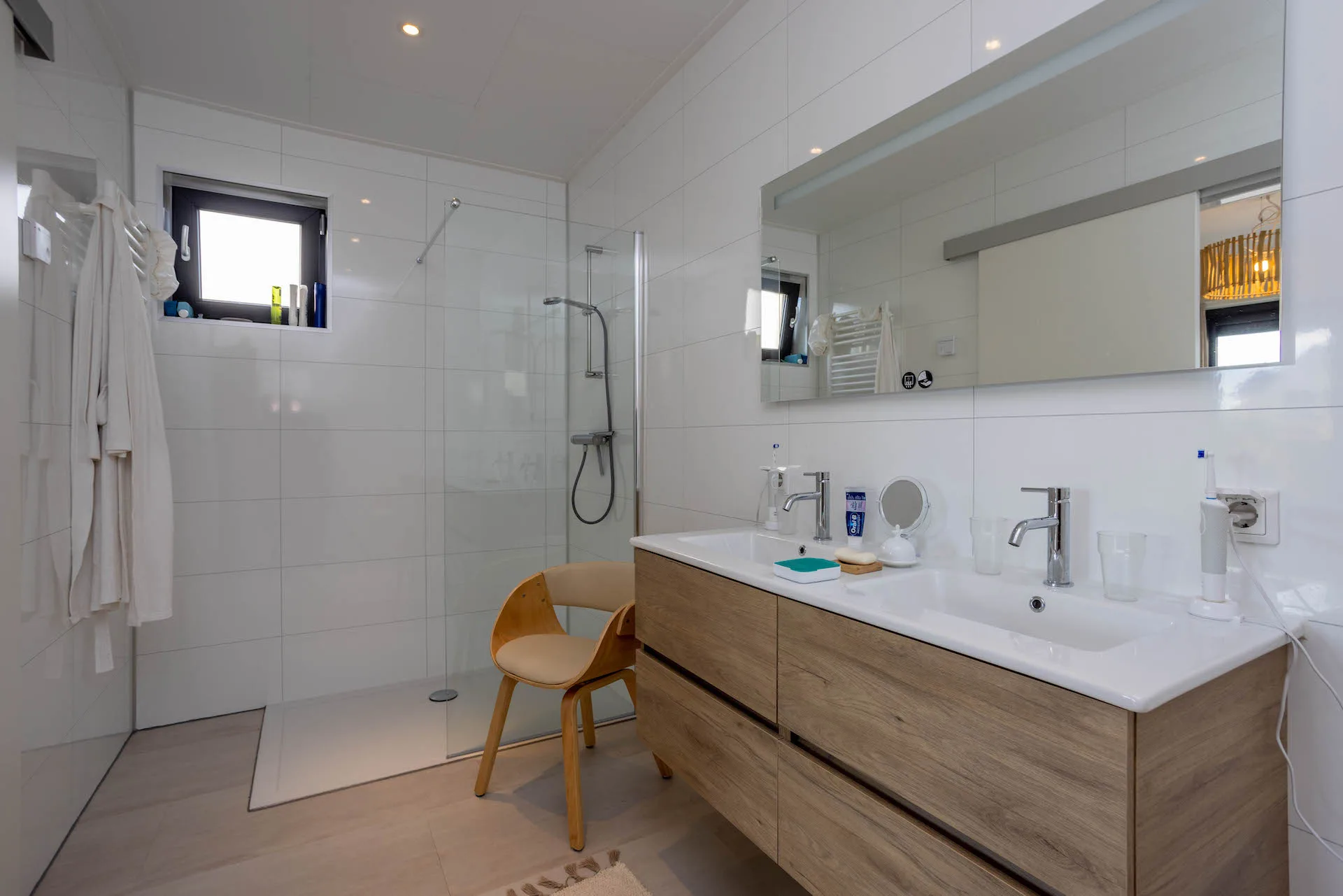 Strakke glazen douchewand in een lichte badkamer met houten wastafelmeubel